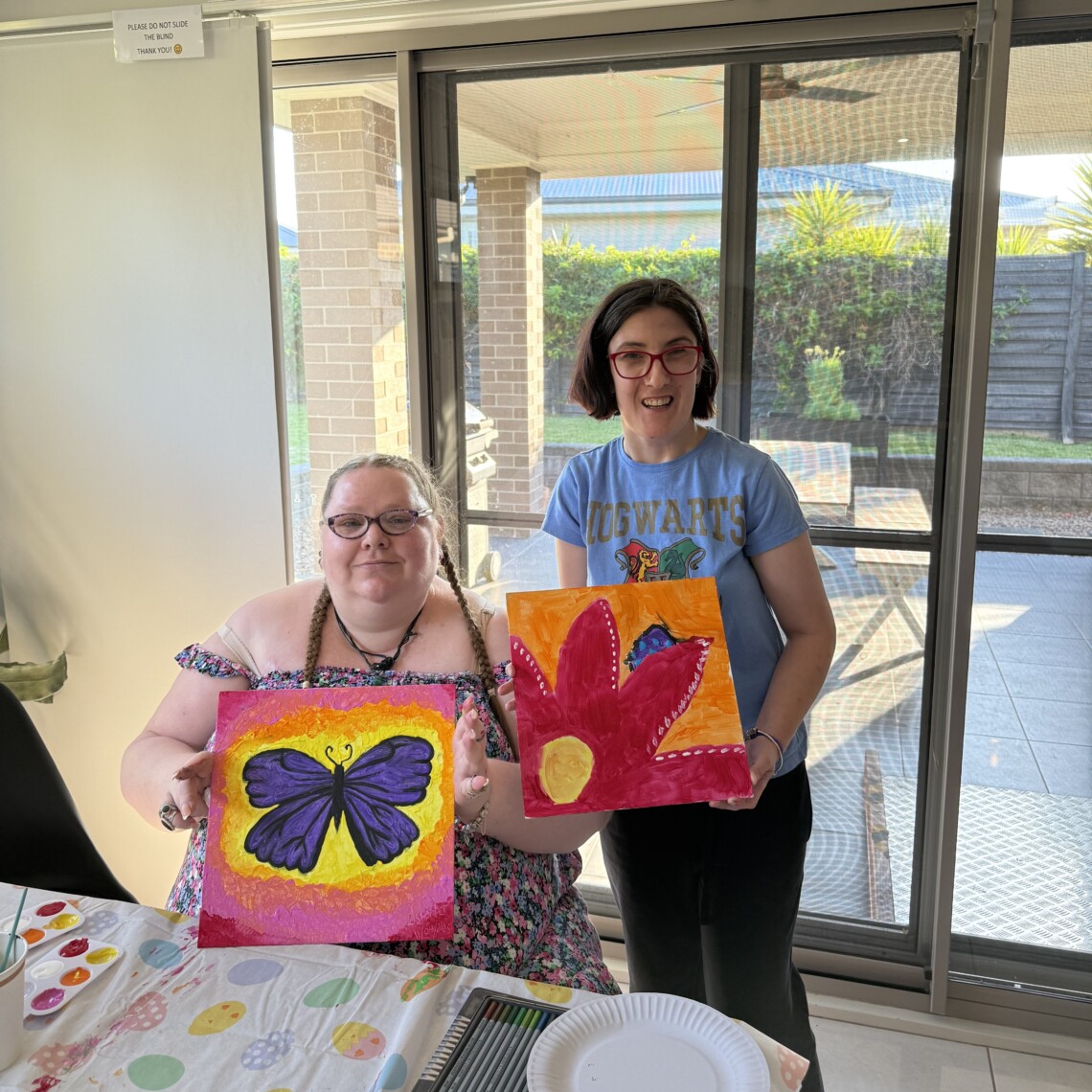 Two people showing off their paintings of a butterfly and a flower.